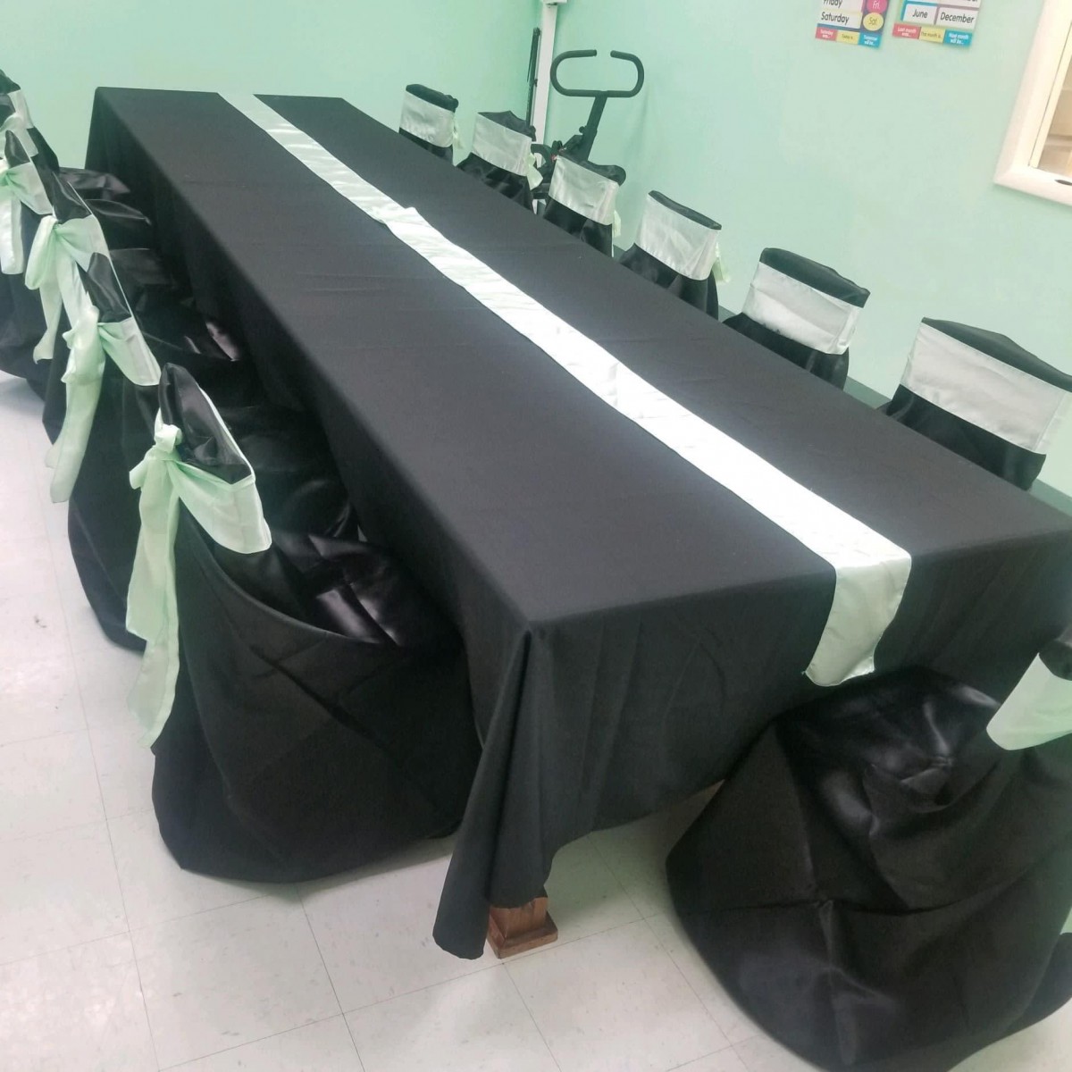 A neatly arranged table with black cloth and white runner, accompanied by black chair covers in an indoor setting.