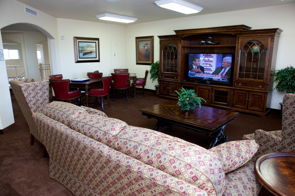 A cozy living room featuring a floral sofa, a wooden entertainment center with a television, and a set of red chairs around a small table.