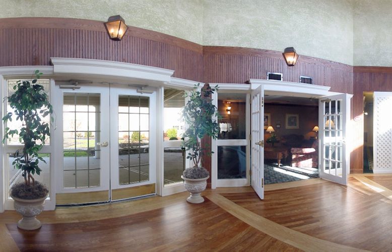 A spacious lobby with glass doors, warm lighting, and wooden flooring.