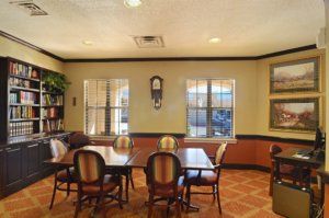 A cozy dining area with wooden tables and chairs, featuring large windows and a wall clock.