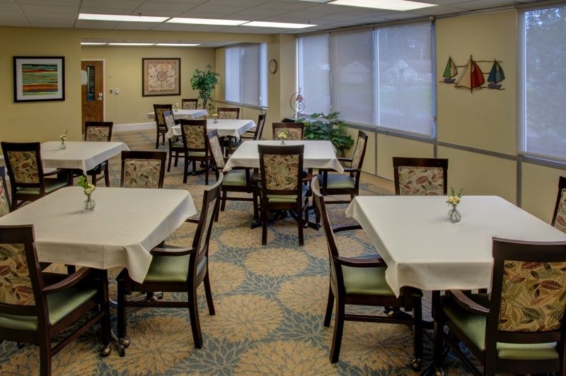 An empty dining room with tables covered in white tablecloths, surrounded by chairs and decorated with indoor plants.