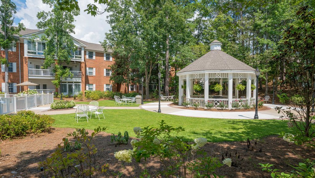 A serene garden area with a gazebo, surrounded by trees and a nearby building.