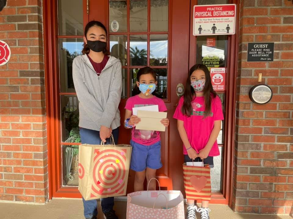 Three people standing in front of a door, wearing masks and holding shopping bags.