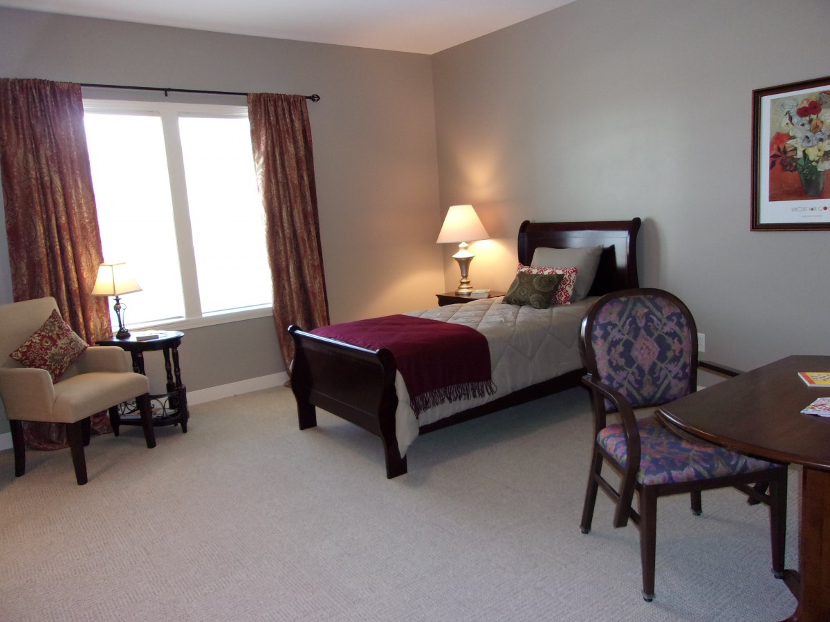 A cozy bedroom with a single bed, lamp, and window with curtains.