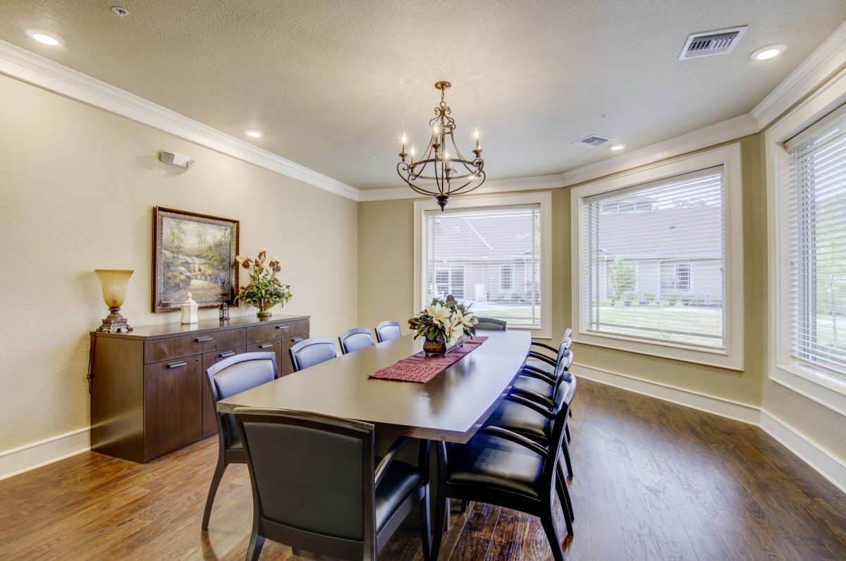 A well-lit dining room featuring a large table with chairs, a chandelier, and large windows.