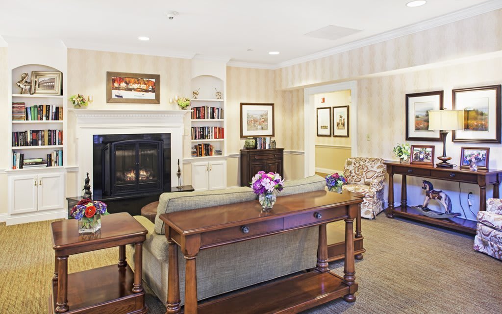 A cozy living room with a fireplace, sofa, and bookshelf adorned with flowers and decorative elements.