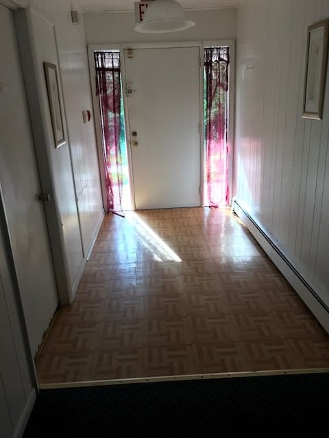 A hallway with a wooden floor and sunlight streaming through the door.