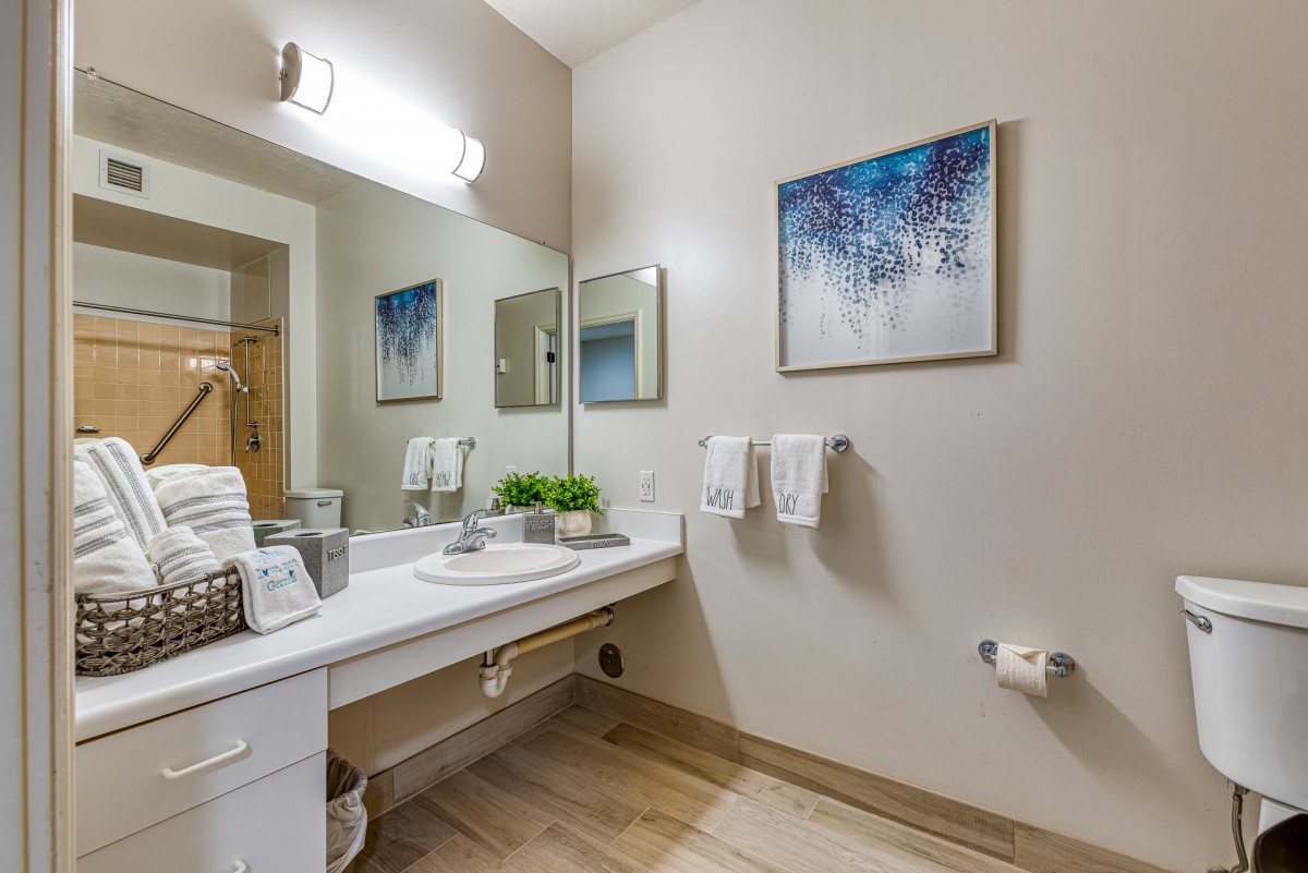 A modern bathroom with a clean countertop, mirror, and wall art.