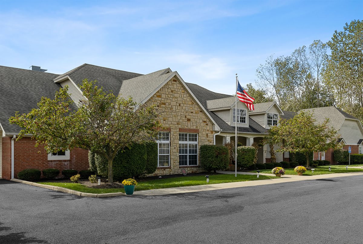 A suburban residential house with a stone and brick exterior, surrounded by trees and featuring an American flag.