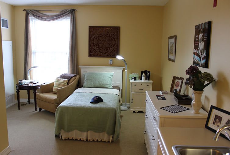 A cozy bedroom with a single bed, a lamp, and a comfortable chair by the window.