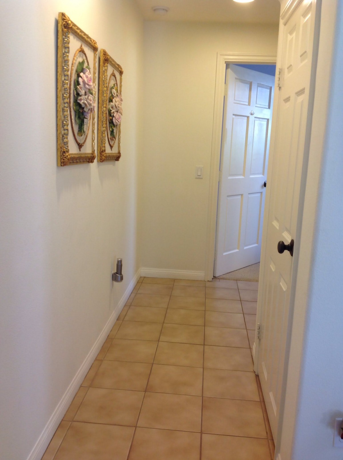 A tiled hallway with framed artwork on the walls leading to a doorway.