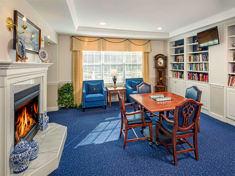 A cozy living room with a fireplace, armchairs, and a dining table surrounded by bookshelves.
