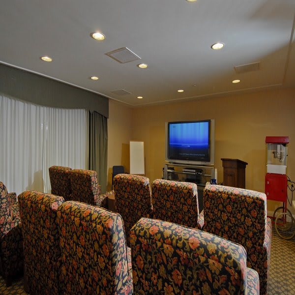 A cozy home theater setup with rows of upholstered seating facing a large TV, complete with a popcorn machine in the corner.