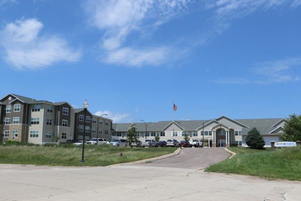 A large residential building with a driveway, surrounded by an open grassy area under a blue sky.