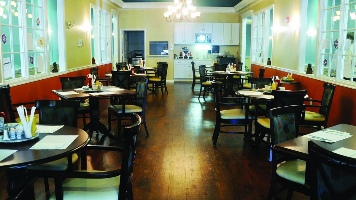 An empty restaurant dining area with arranged tables and chairs, featuring a chandelier.