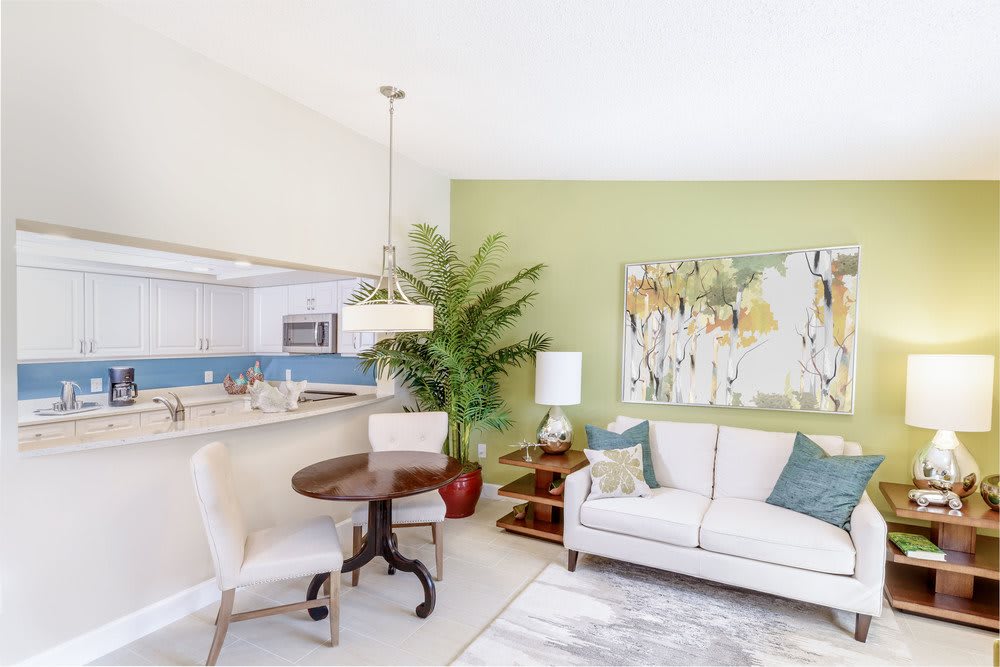 A modern living room with a light-colored sofa, decorative cushions, a small round dining table, and an indoor plant.