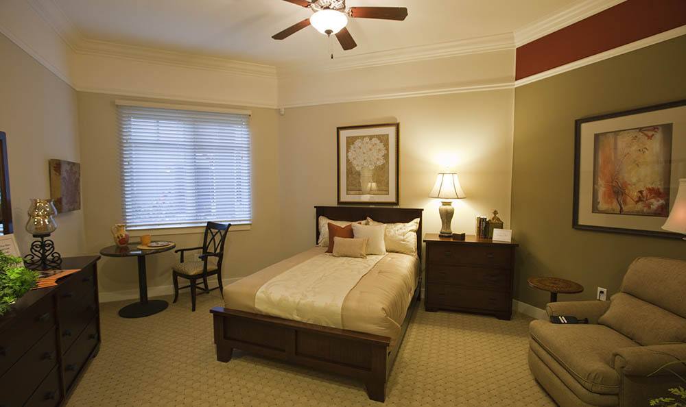 A cozy bedroom featuring a neatly made bed, wooden furniture, and a ceiling fan.