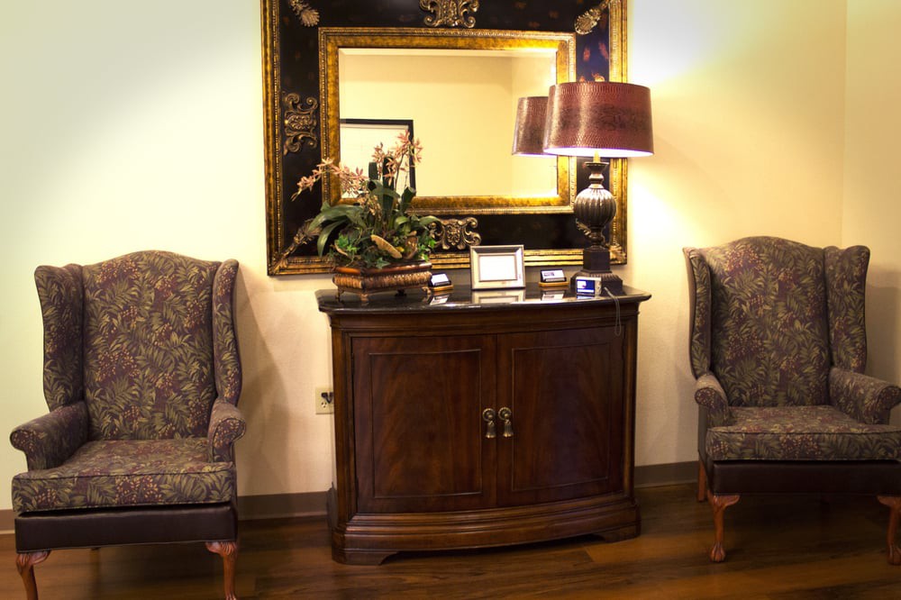 A classic interior setup featuring a wooden cabinet, large mirror, and two upholstered chairs.