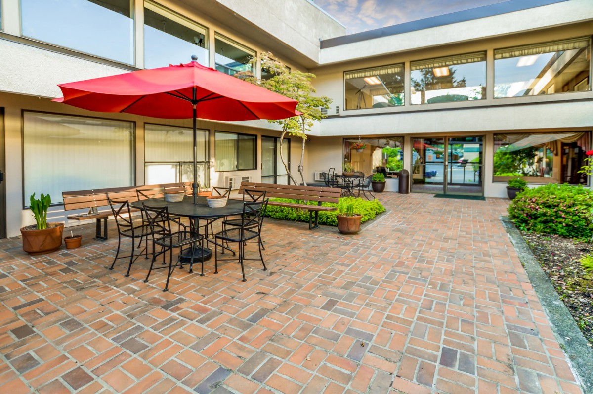 Outdoor patio area with tables, chairs, and a red umbrella on brick flooring.