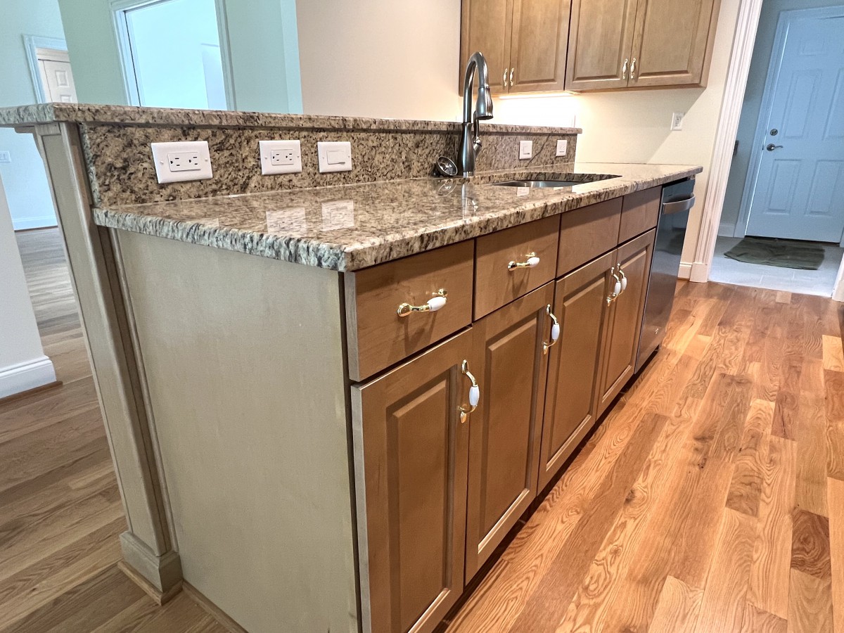 A modern kitchen with granite countertops, wooden cabinets, and a hardwood floor.