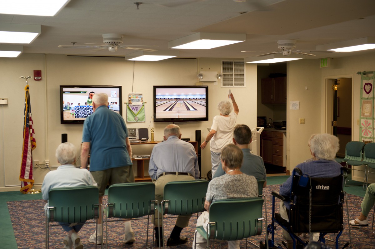 A group of seniors enjoying a game of Wii bowling in a communal indoor setting.