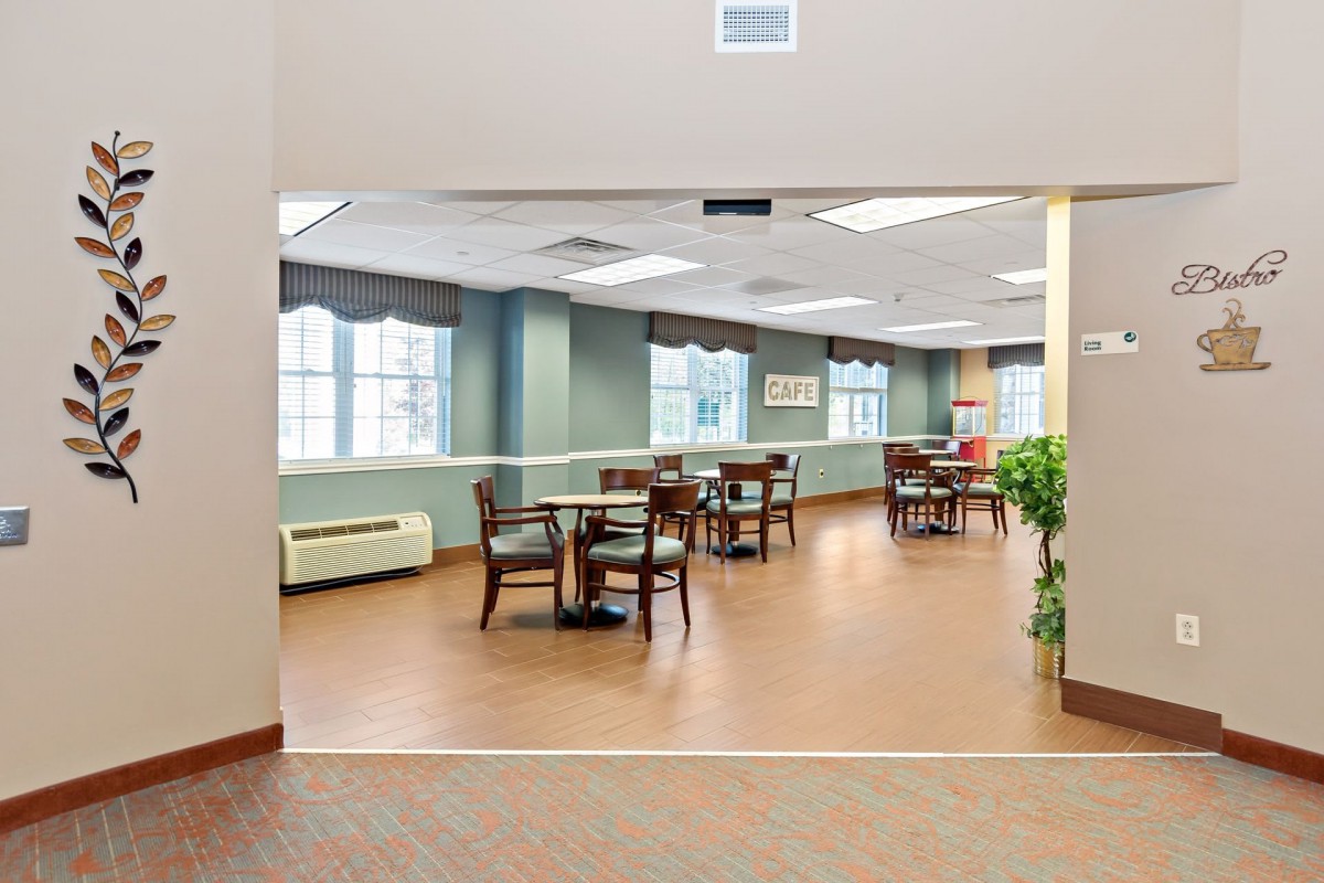 A well-lit dining area with tables and chairs, featuring large windows and a simple decor.
