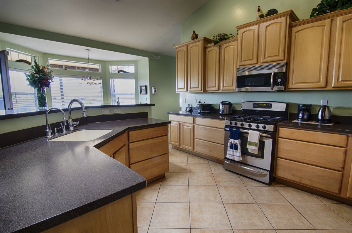 A modern kitchen interior featuring light wood cabinets, dark countertops, and stainless steel appliances.