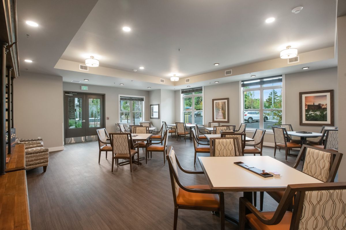 A modern dining area with multiple tables and chairs, featuring large windows and elegant lighting.