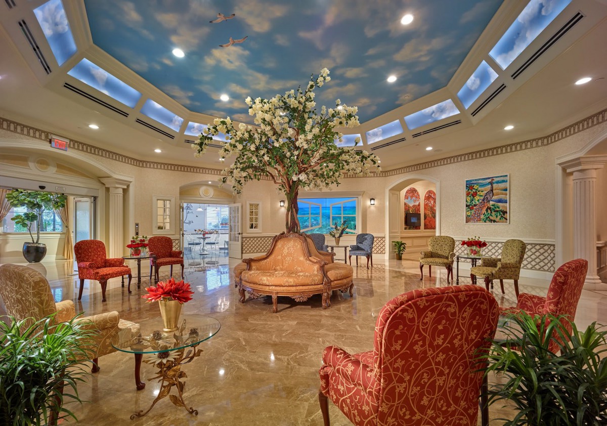 A beautifully decorated lobby with an artificial tree centerpiece and elegant seating arrangements, featuring a sky-themed ceiling mural.