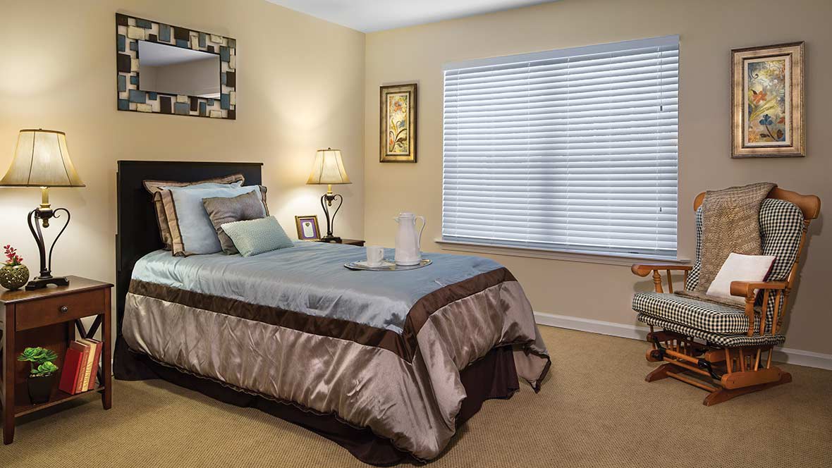 A cozy bedroom with a neatly made bed, soft lighting, and a large window.