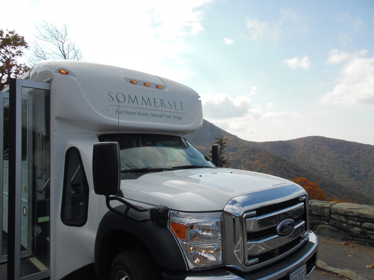 A bus parked in a scenic mountainous area under a partly cloudy sky.