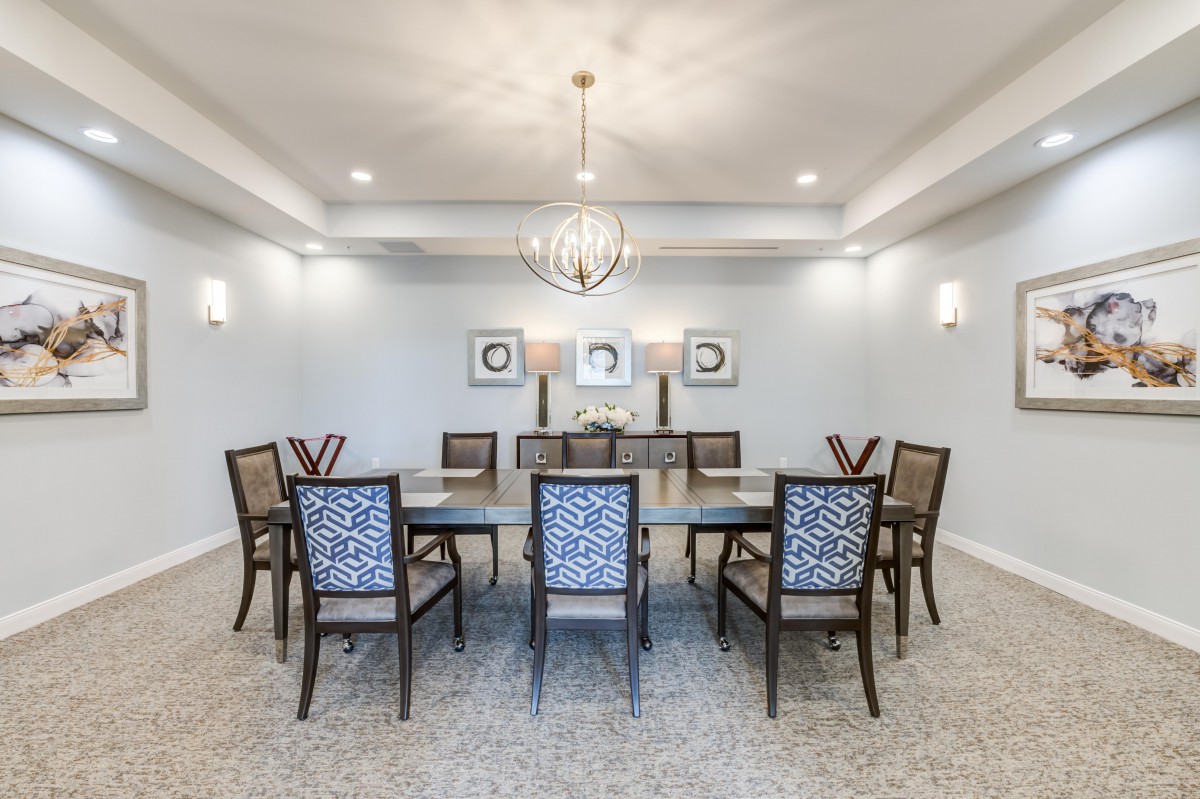 A spacious dining room with a large table and elegant chairs, featuring a modern chandelier and wall decorations.
