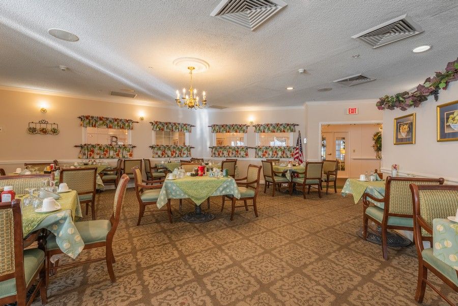 An elegantly decorated dining room with several tables and chairs, featuring a chandelier and carpeted flooring.
