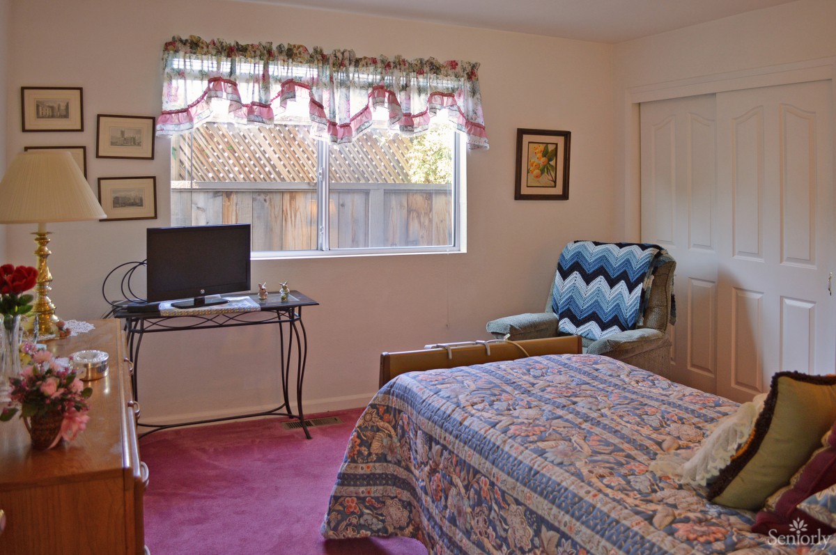 Cozy bedroom with a TV, armchair, and a patterned quilt on the bed.