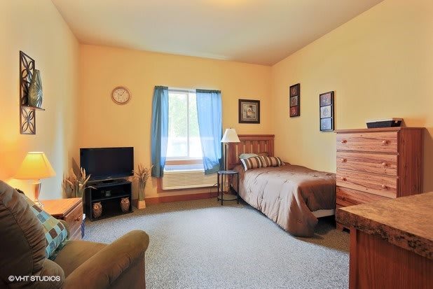 A cozy bedroom with a single bed, television, and wooden furniture.