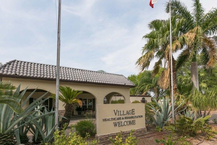 Entrance to a community center with tropical landscaping and flags.
