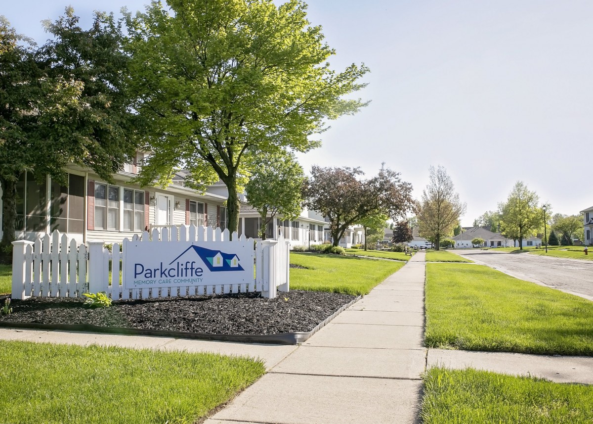 A peaceful residential area with apartments, a well-maintained lawn, and a sidewalk lined with trees.