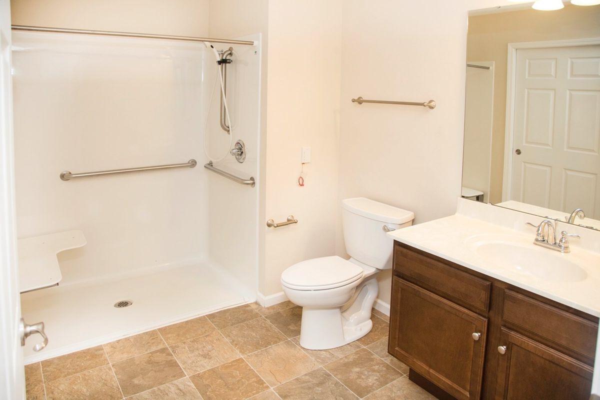 A clean and spacious bathroom featuring a shower, toilet, and sink with tiled flooring.