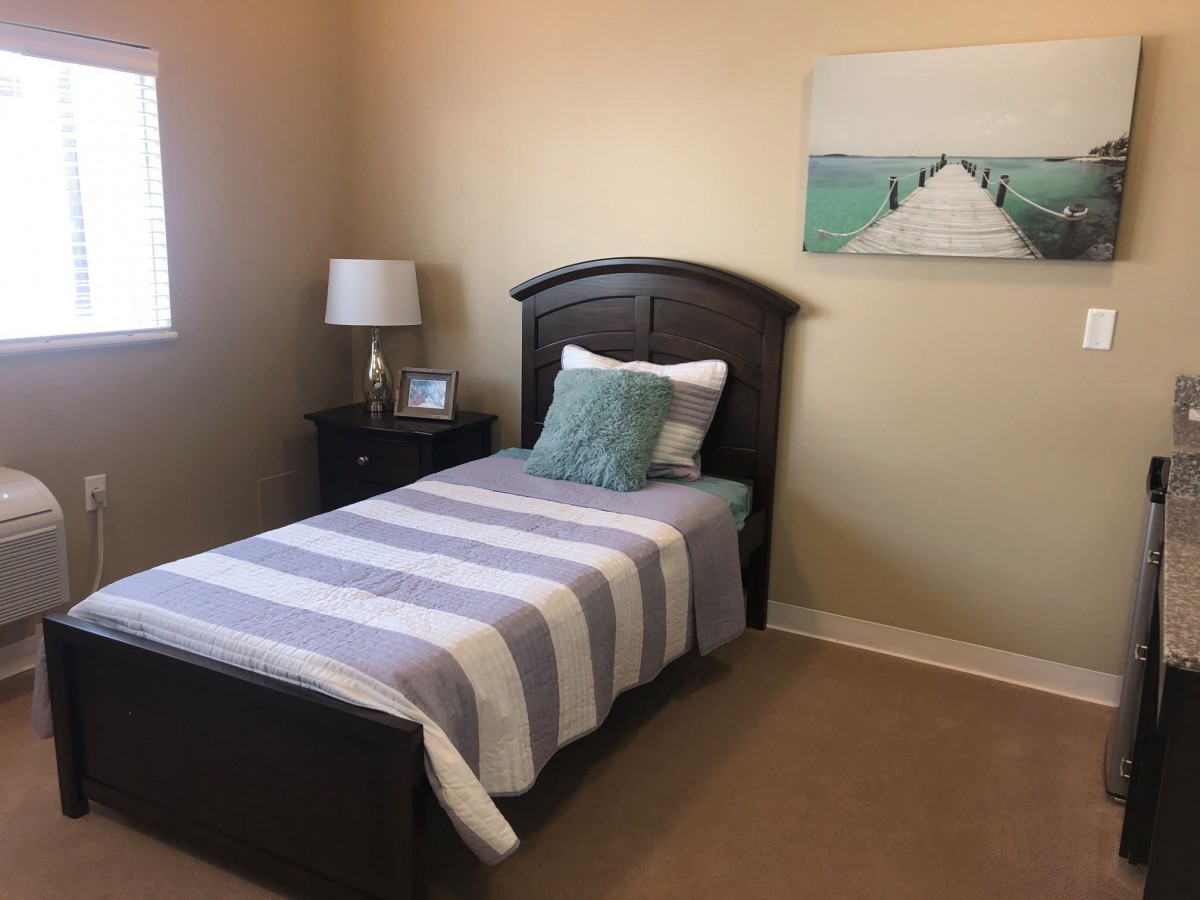 A cozy bedroom with a single bed featuring striped bedding, complemented by a nightstand with a lamp and soothing wall art.
