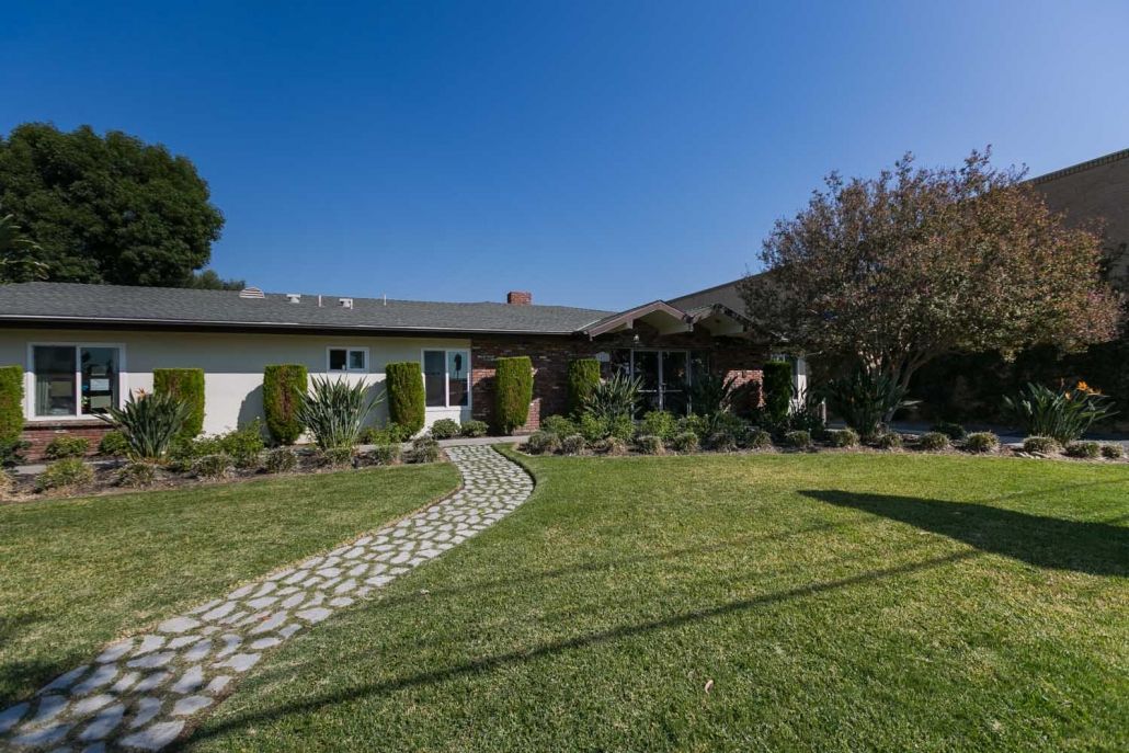A charming suburban house with a well-maintained lawn and garden under a clear blue sky.