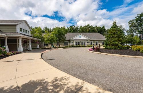 A scenic view of a building with a circular driveway, surrounded by trees and a partly cloudy sky.