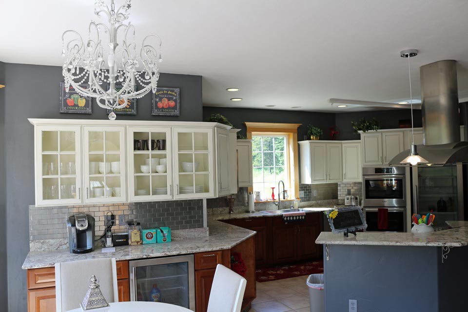 A modern kitchen with white cabinets, elegant chandelier, and ample natural light.