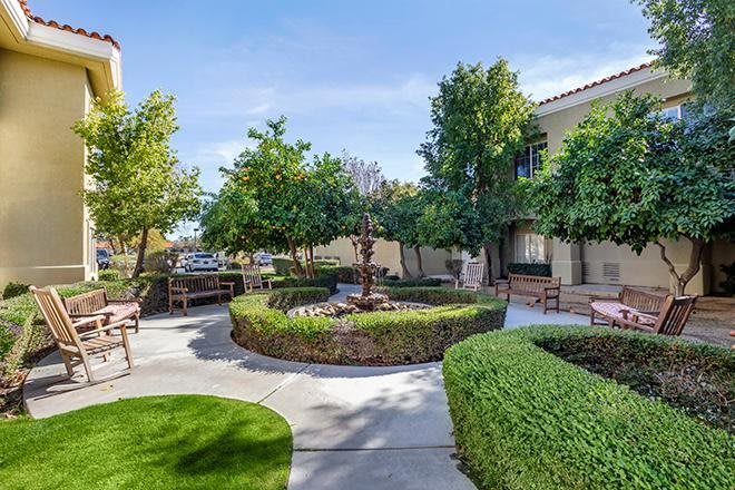 A beautifully landscaped courtyard with manicured shrubs, trees, and benches along a winding pathway.