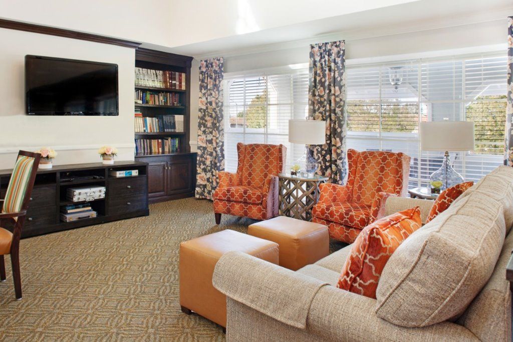 A cozy living room with vibrant orange accents, featuring a comfortable sofa, armchairs, a television, and a well-stocked bookshelf.