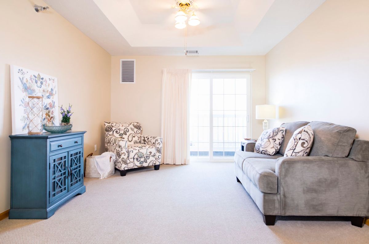 A brightly lit living room featuring a comfortable sofa, patterned armchair, and a blue dresser against neutral walls.