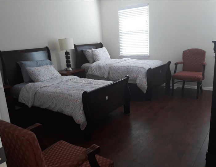 A bedroom with two twin beds, chairs, and a window.