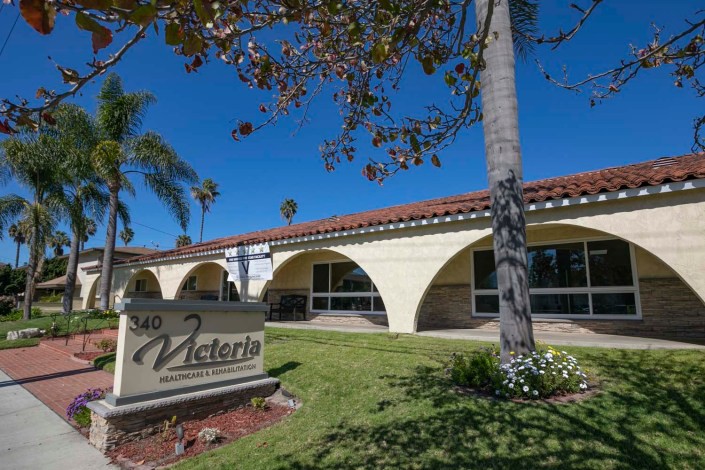 A sunny day at a building with distinct arched architecture and palm trees, featuring a sign in the foreground.