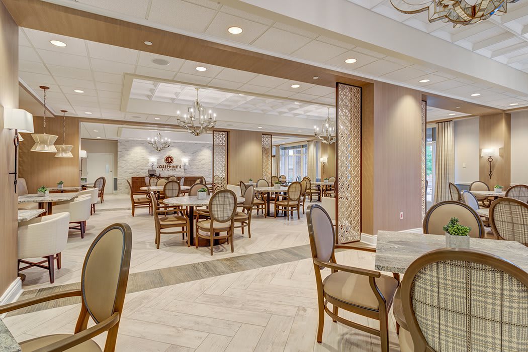 An elegant dining area with neatly arranged tables and chairs, illuminated by chandeliers.