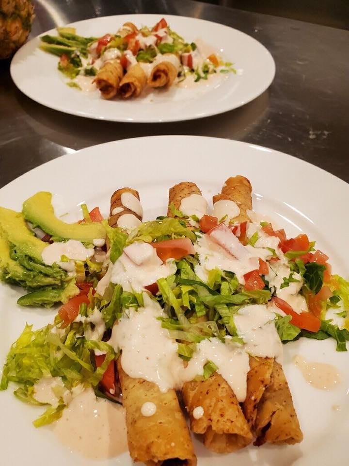 A plate of taquitos garnished with crema, fresh vegetables, and slices of avocado.