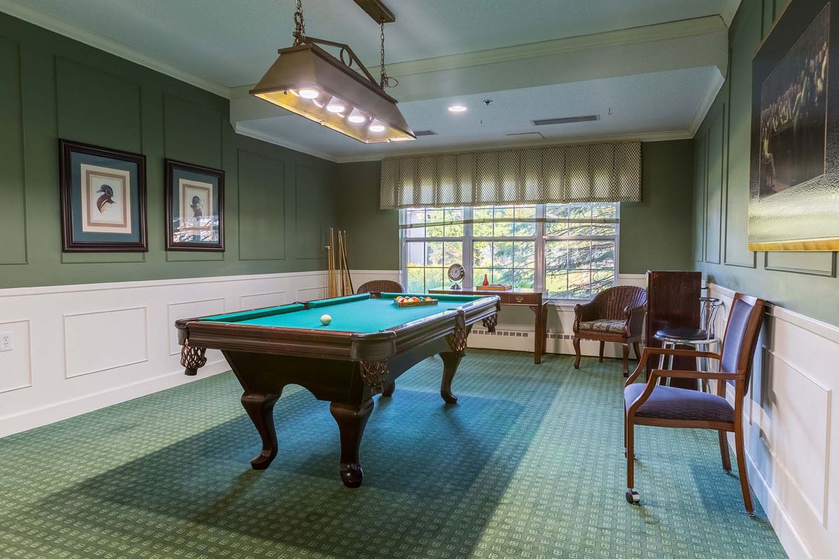 A cozy billiard room featuring a pool table, chairs, and green-themed decor.